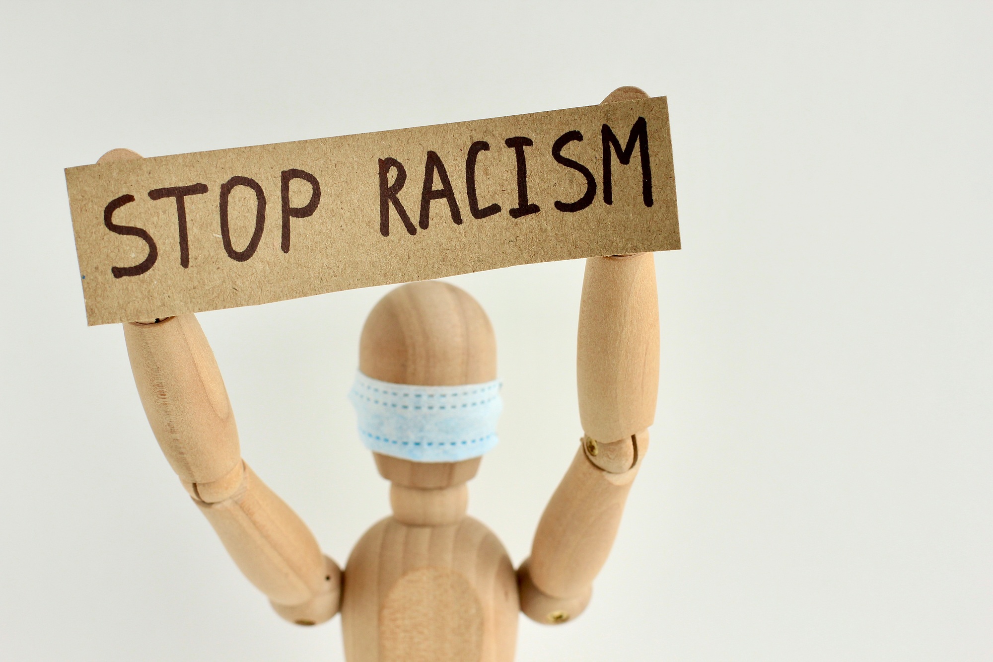 Cardboard sign with text stop racism in the hands of mannequin in a medical mask. Anti xenophobia.